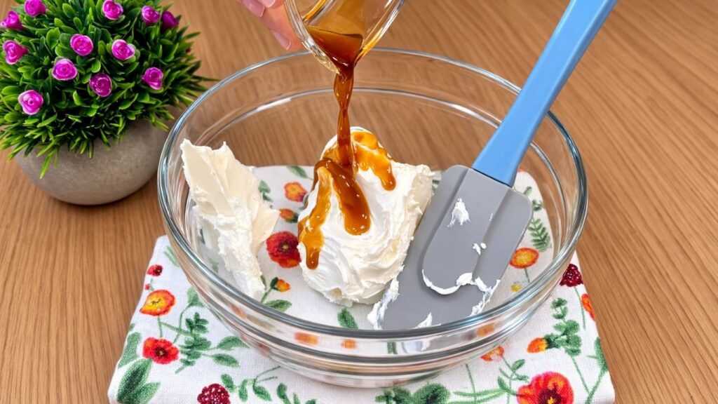 pouring vanilla extract over cream cheese while preparing frosting for blueberry lemon rolls