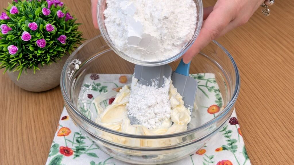 adding powdered sugar to the cream cheese frosting for blueberry lemon rolls