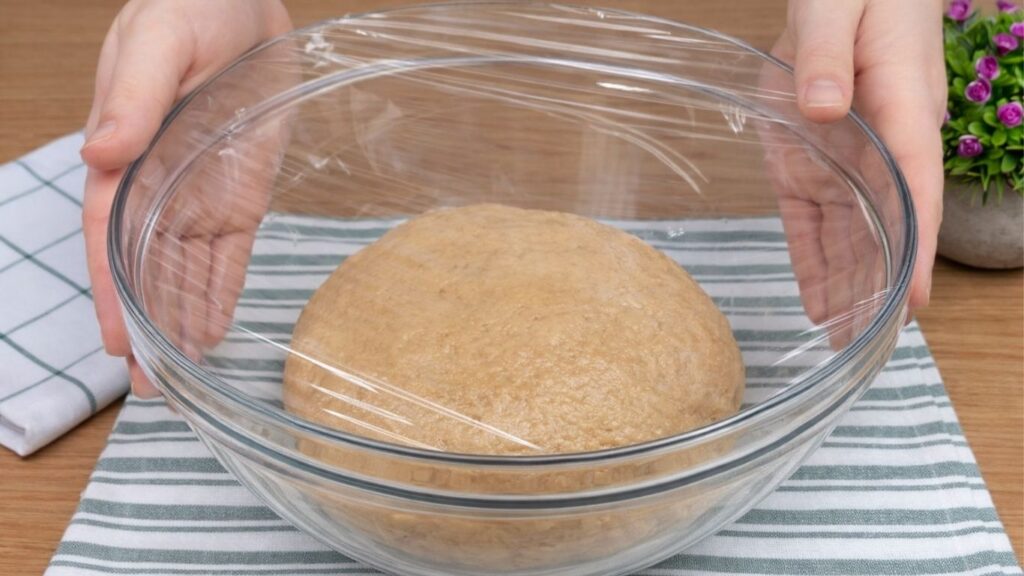 Bowl of apple cinnamon roll dough covered with plastic wrap and left to rise.