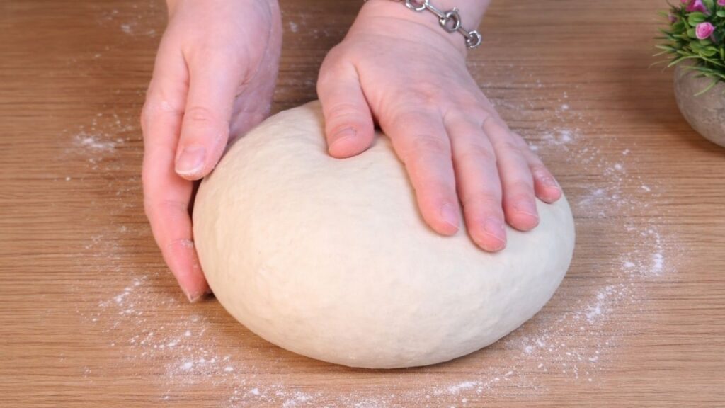 Smooth and elastic dough for homemade hot dog buns on a floured work surface after kneading.