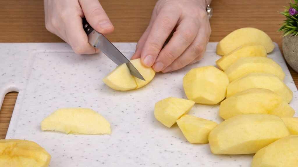 Dicing peeled apples into small cubes on a white cutting board for apple cinnamon roll filling.