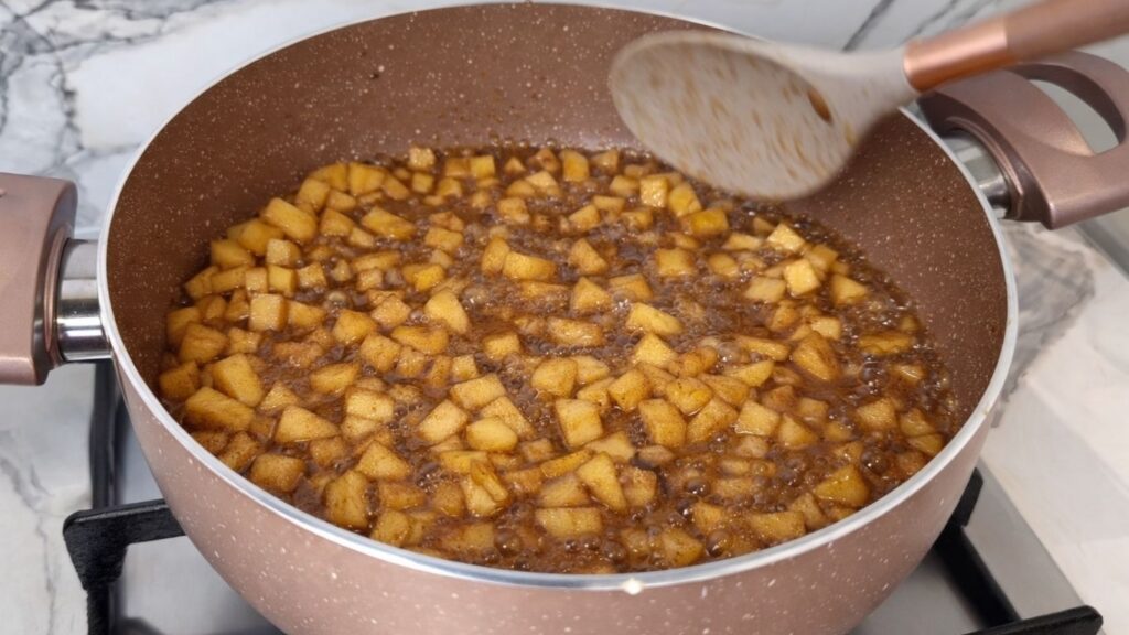 Apple cinnamon filling cooking in a saucepan as the diced apples soften with sugar and cinnamon.