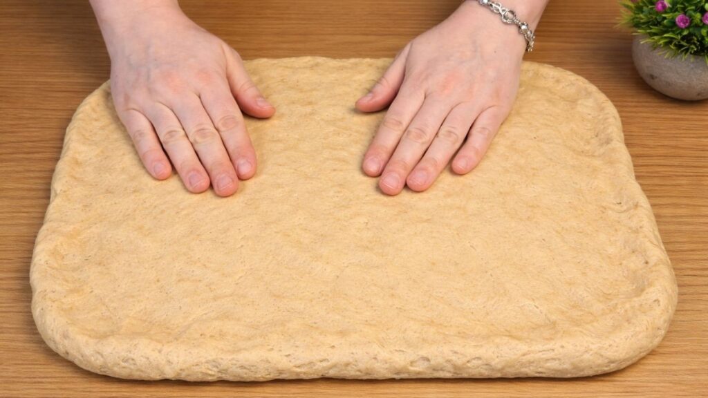 Apple cinnamon roll dough stretched into a large rectangle on a work surface, ready for filling.