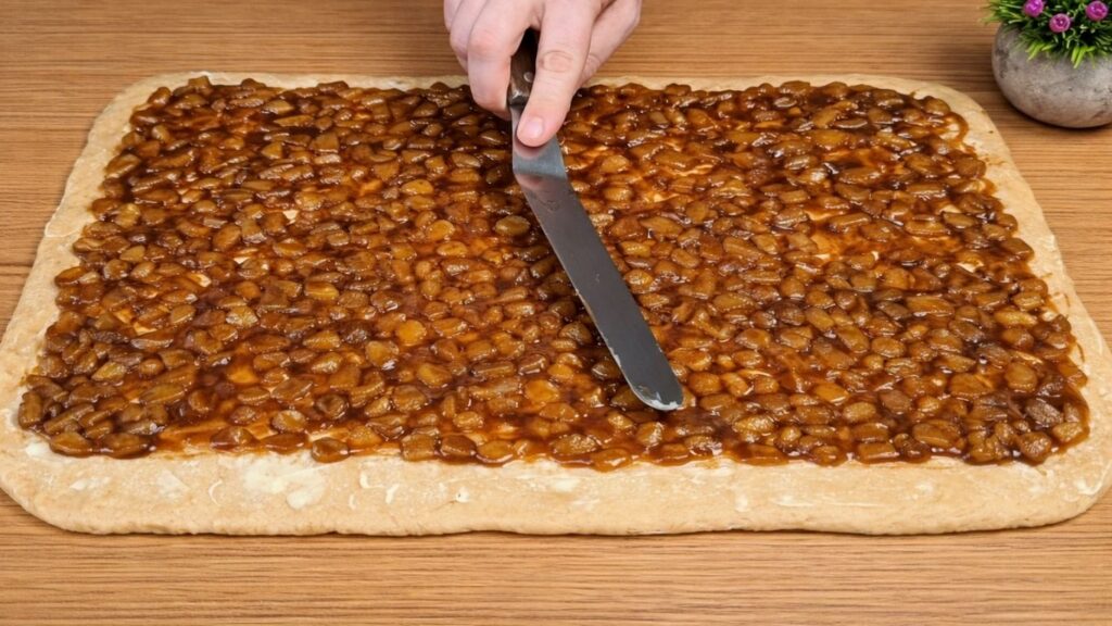 Apple cinnamon filling evenly spread across the dough before shaping the rolls.