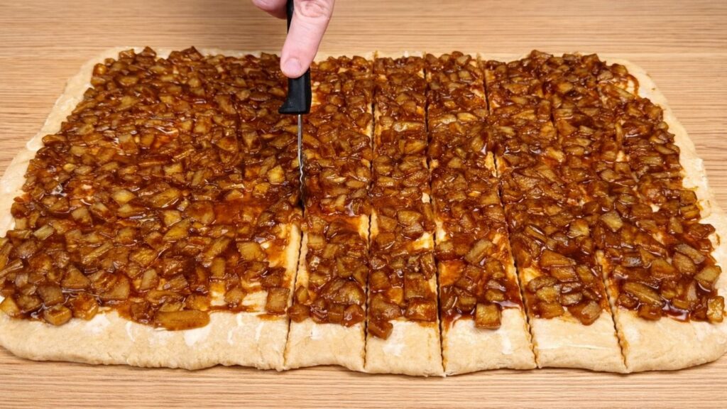 Dough with apple cinnamon filling cut into long strips for shaping apple cinnamon rolls.