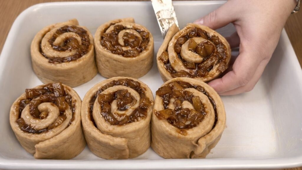 Placing shaped apple cinnamon rolls into a baking dish before baking.