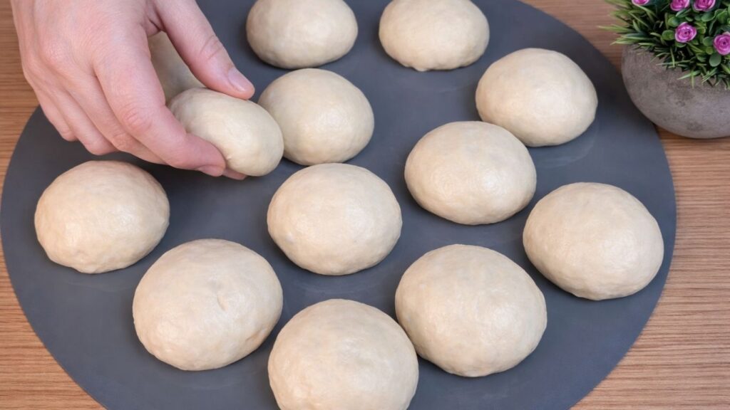 Shaped dough balls arranged on a silicone mat while preparing homemade hot dog buns.