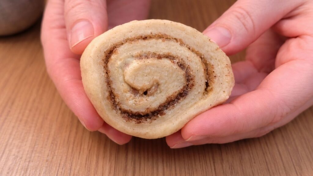 freshly cut cinnamon roll held in hands showing soft layers