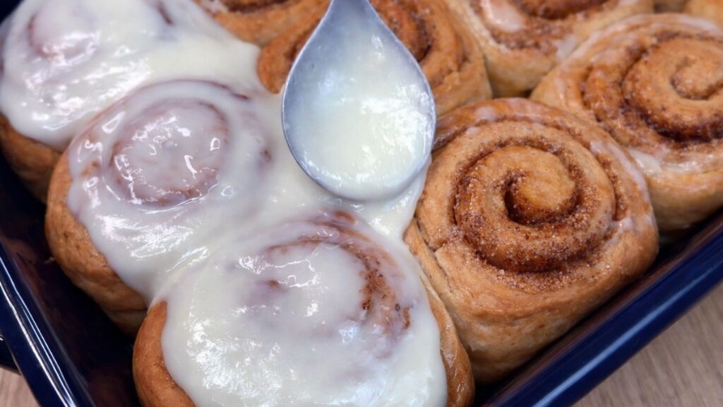spreading cream cheese glaze over warm homemade cinnamon rolls