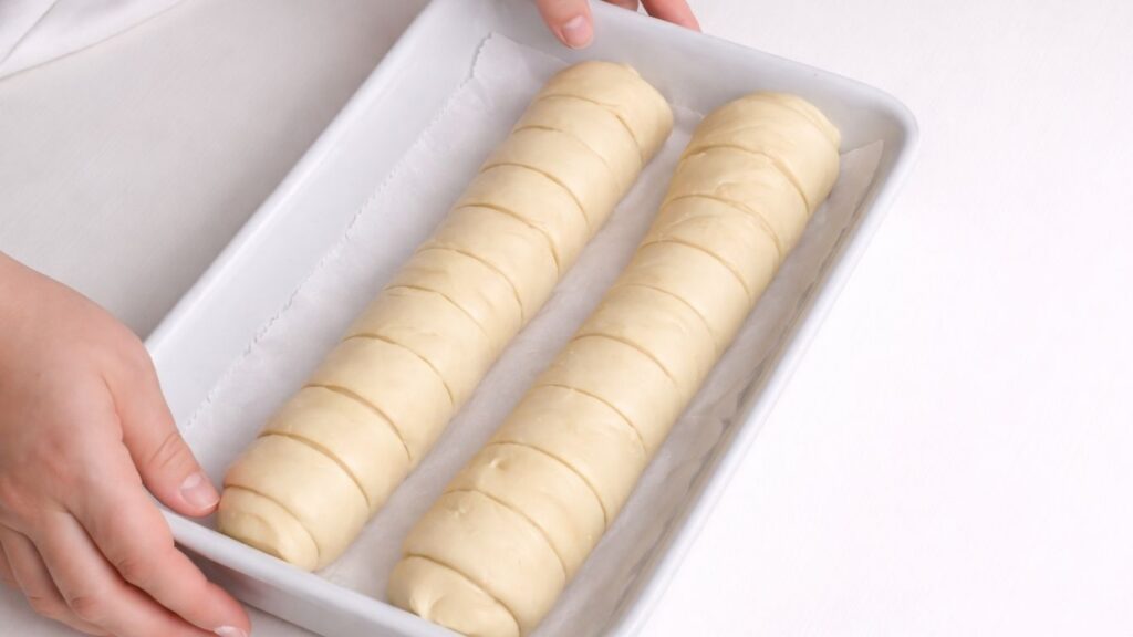 shaped milk bread loaves rising in a ceramic baking dish