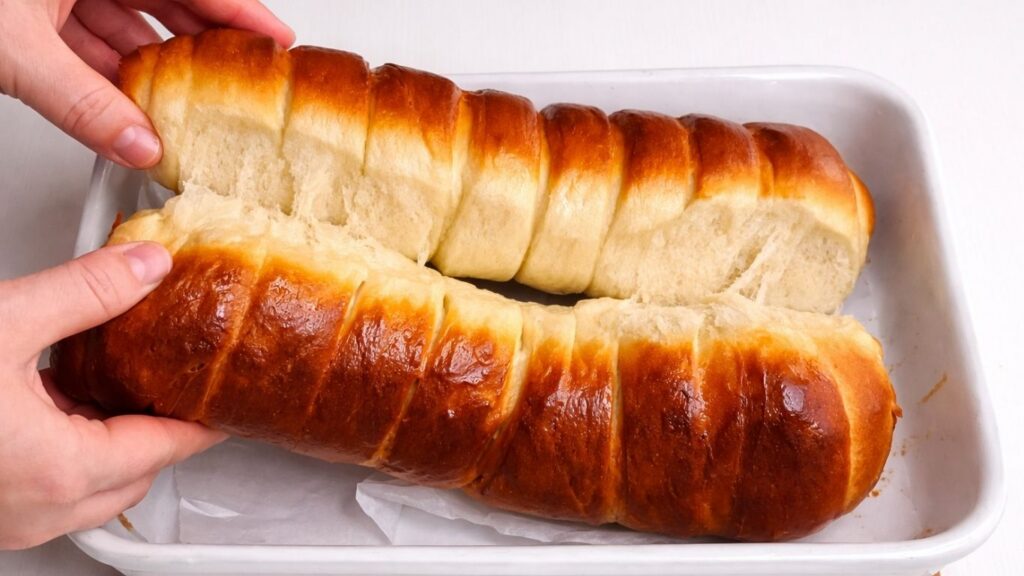 separating two milk bread loaves in a ceramic baking dish