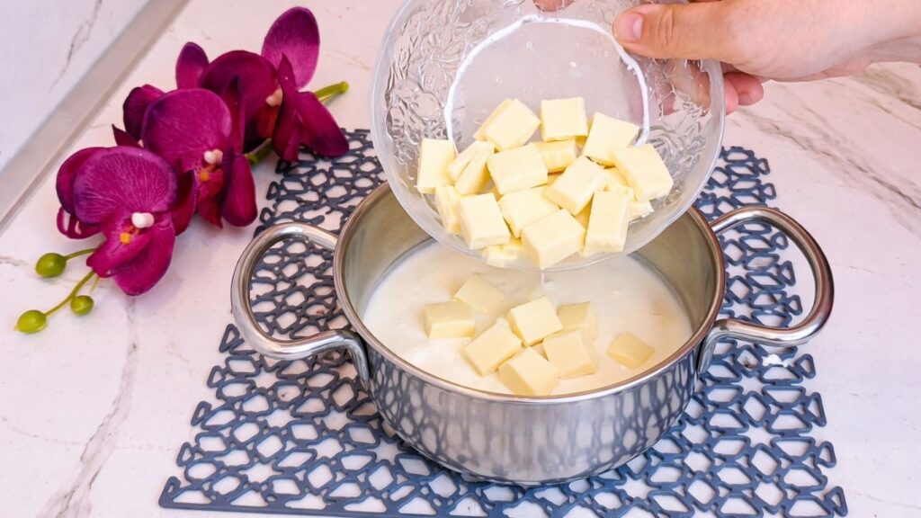 Adding white chocolate to heavy cream in saucepan for pistachio ganache