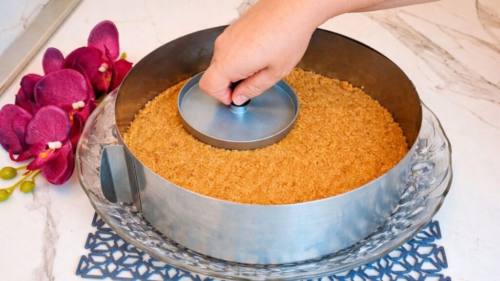 Pressing cookie crust evenly into cake pan for no bake pistachio cake