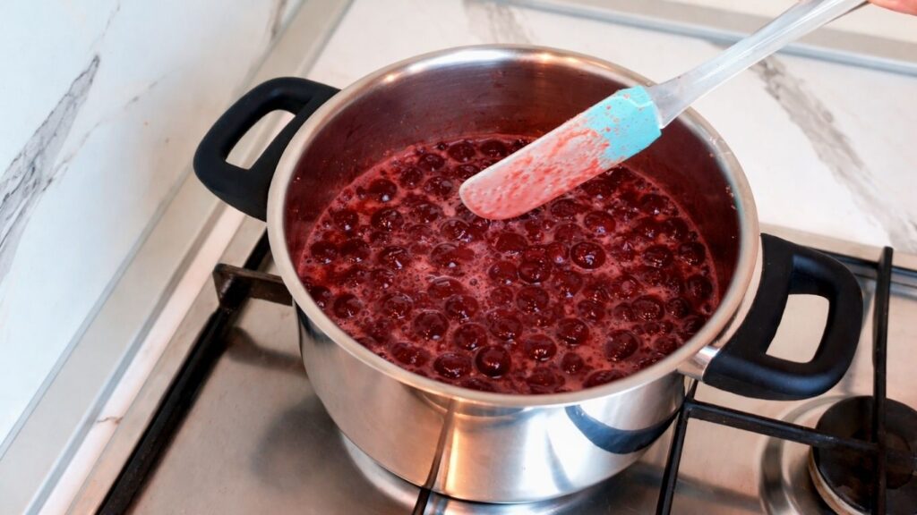 Boiling cherries in saucepan for cherry layer of pistachio cake