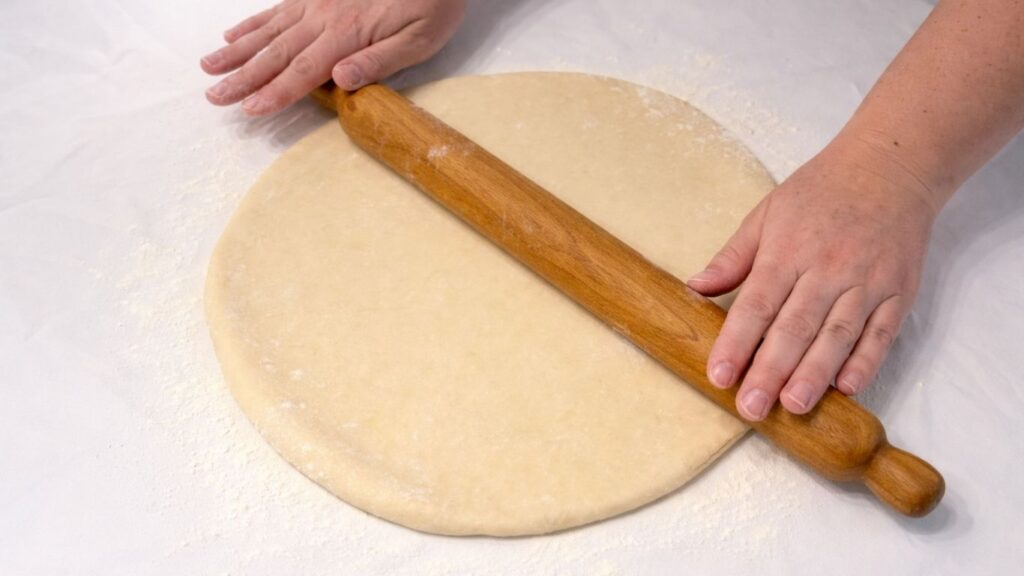 rolling potato borek dough with a rolling pin on a floured surface