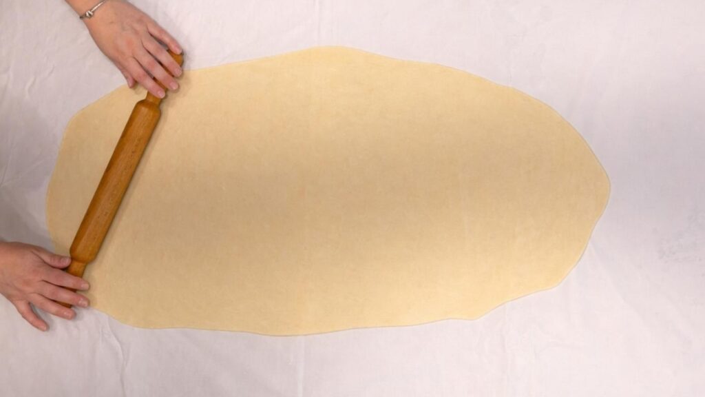 rolling potato borek dough with a rolling pin on a floured surface
