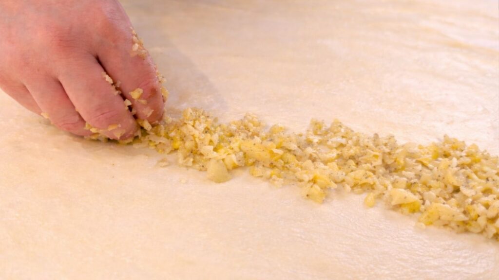 adding potato filling along the edge of stretched dough to make potato borek