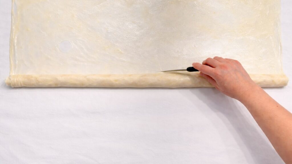 cutting the rolled potato borek dough with a knife to separate the filled section
