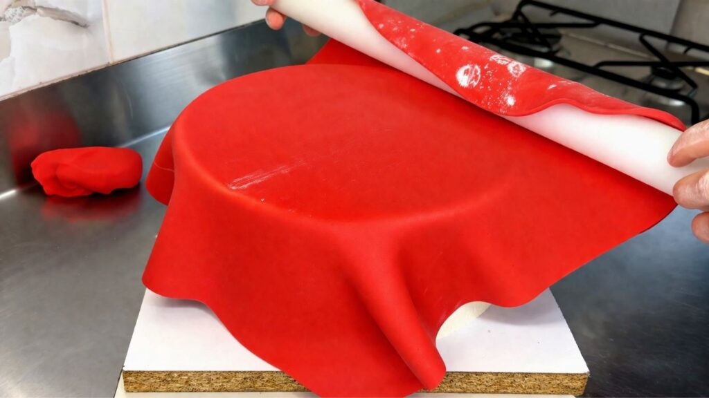 Covering a two-tier 40th birthday cake with red fondant using a rolling pin