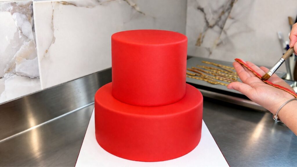 Attaching gold rope border made with Wilton fondant mold on a two-tier red fondant 40th birthday cake