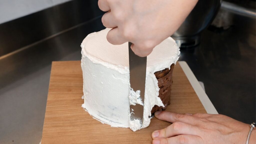 Applying buttercream to the top tier of a 3-tier wedding cake