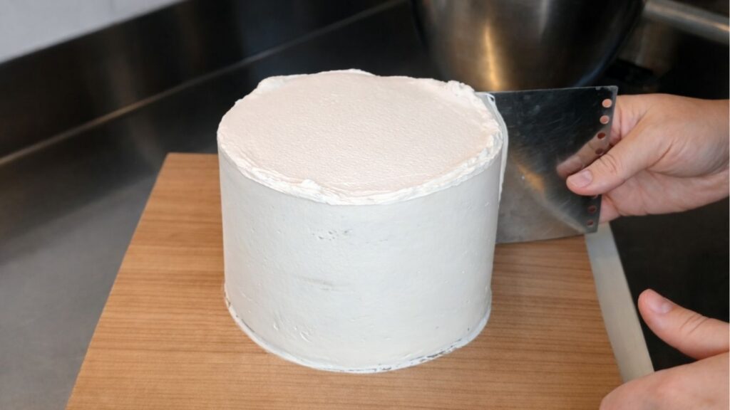 Smoothing buttercream on the top tier of a 3-tier wedding cake