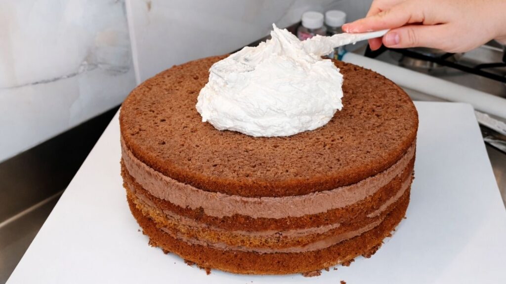 Applying buttercream to the bottom tier of a 3-tier wedding cake