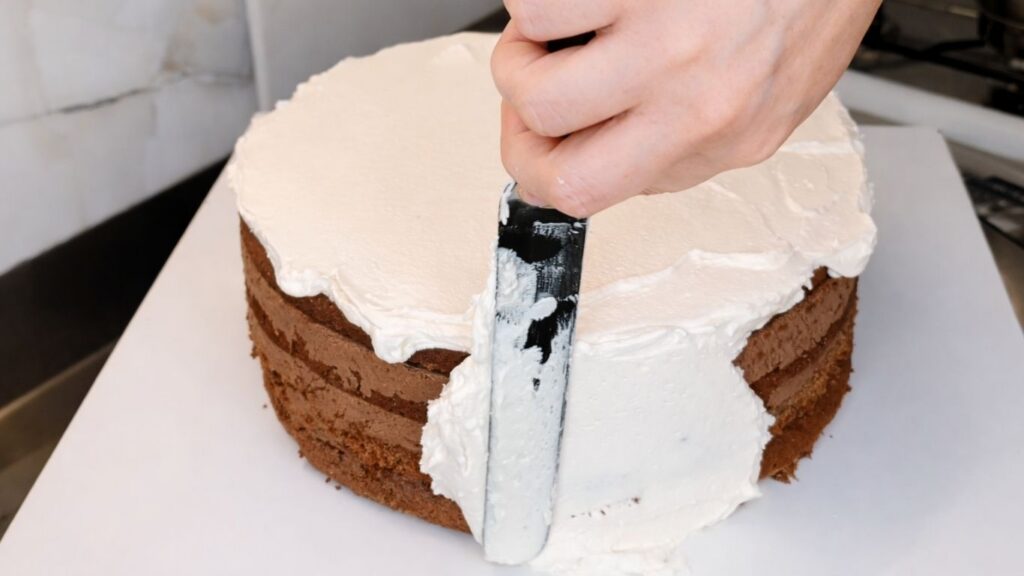 Smoothing buttercream on the bottom tier of a 3-tier wedding cake