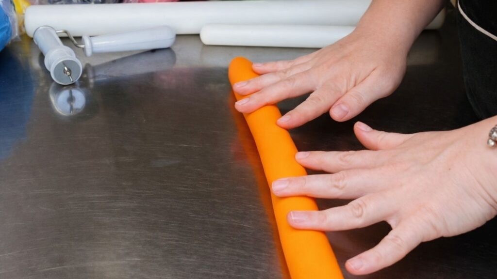 Rolling fondant into a log to prepare it for shaping and cutting candy cake bands.