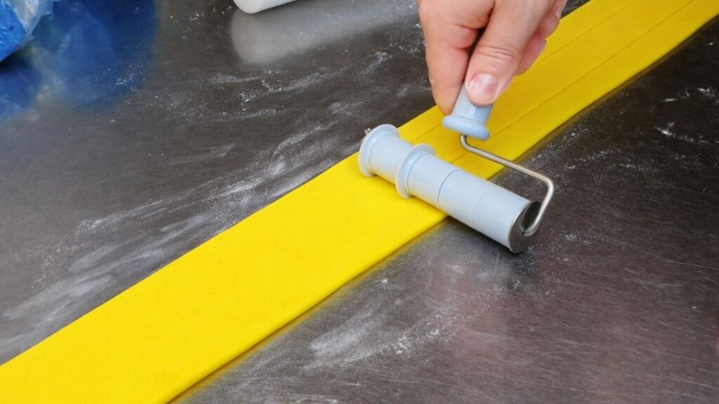 Cutting rolled fondant into even strips with a Wilton strip cutter for the candy cake bands.