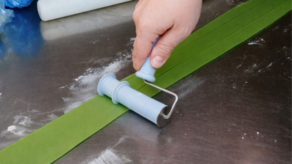 Cutting rolled fondant into even strips with a Wilton strip cutter for the candy cake bands.