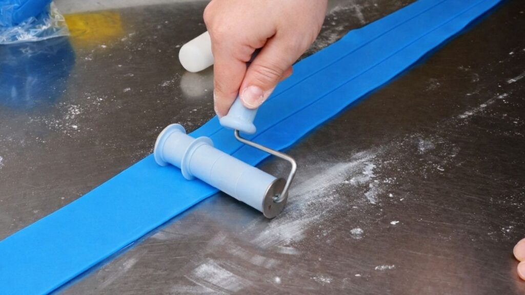 Cutting rolled fondant into even strips with a Wilton strip cutter for the candy cake bands.
