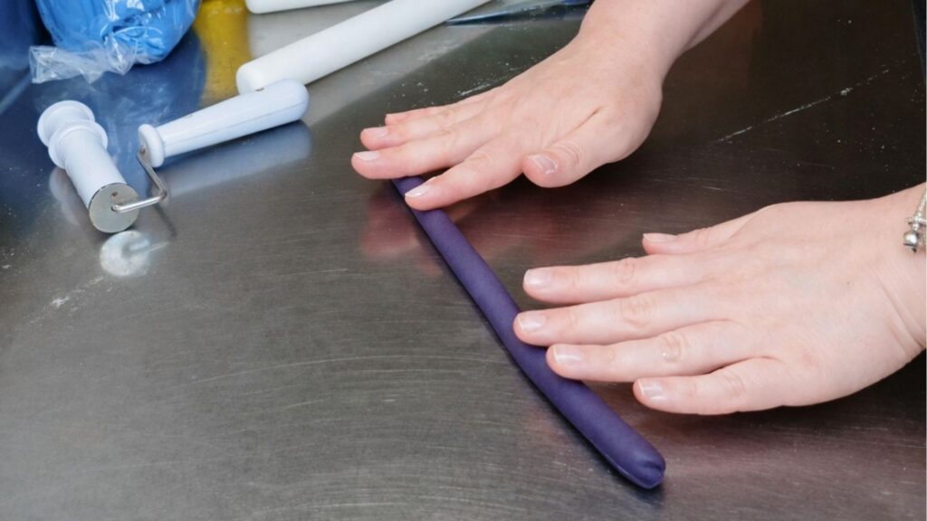 Rolling fondant into a log to prepare it for shaping and cutting candy cake bands.