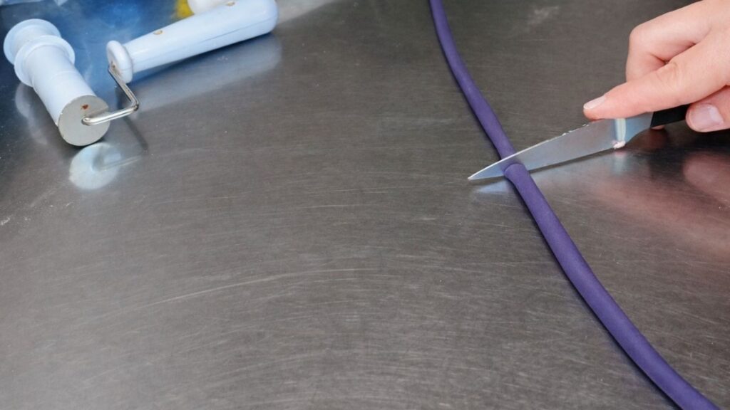 Rolling fondant into a log to prepare it for shaping and cutting candy cake bands.