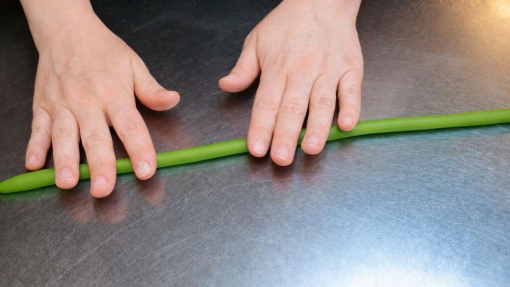 Rolling fondant into a log to prepare it for shaping and cutting candy cake bands.