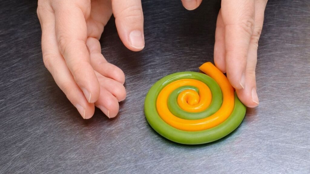 Making a fondant lollipop topper by twisting and coiling two colors for the candy cake.