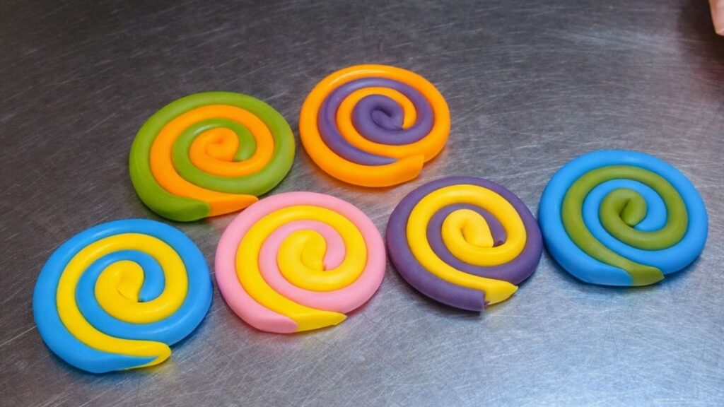 Making a fondant lollipop topper by twisting and coiling two colors for the candy cake.