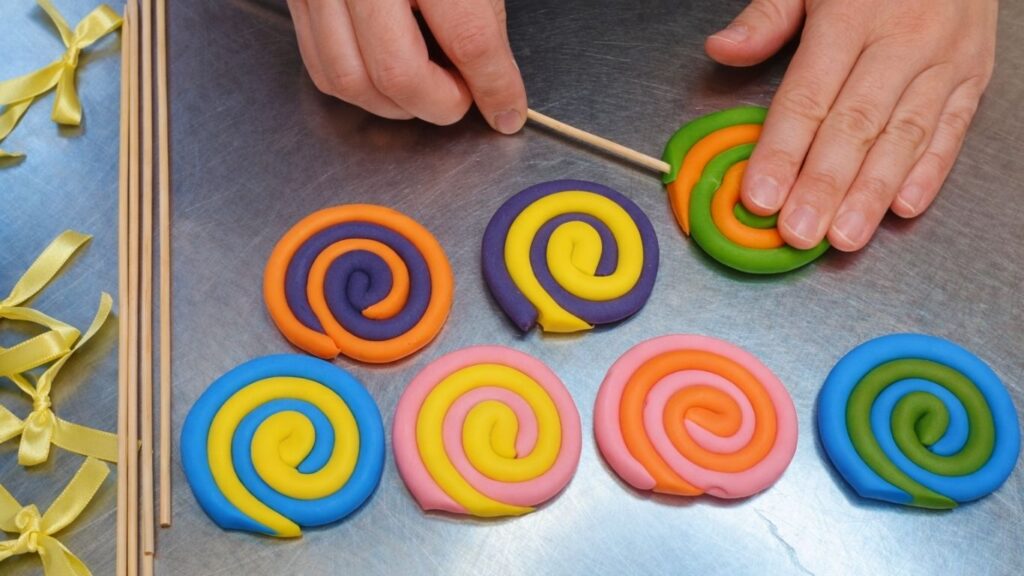 Making a fondant lollipop topper by twisting and coiling two colors for the candy cake.