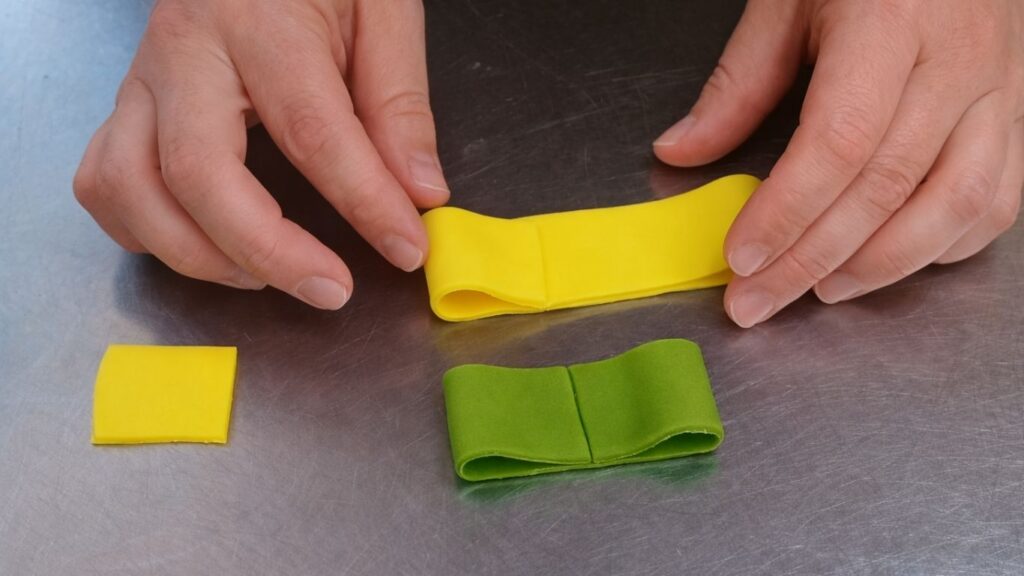 Shaping a fondant bow by folding and pinching strips to decorate the candy cake.