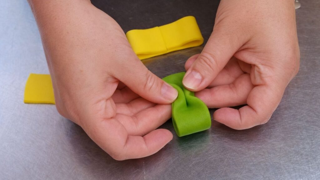 Shaping a fondant bow by folding and pinching strips to decorate the candy cake.