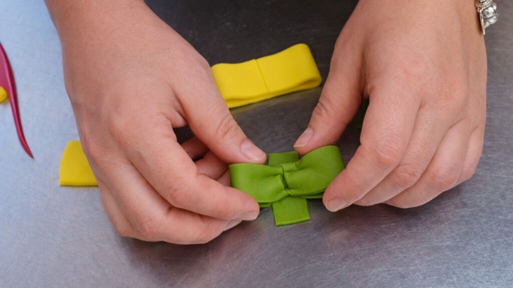 Shaping a fondant bow by folding and pinching strips to decorate the candy cake.