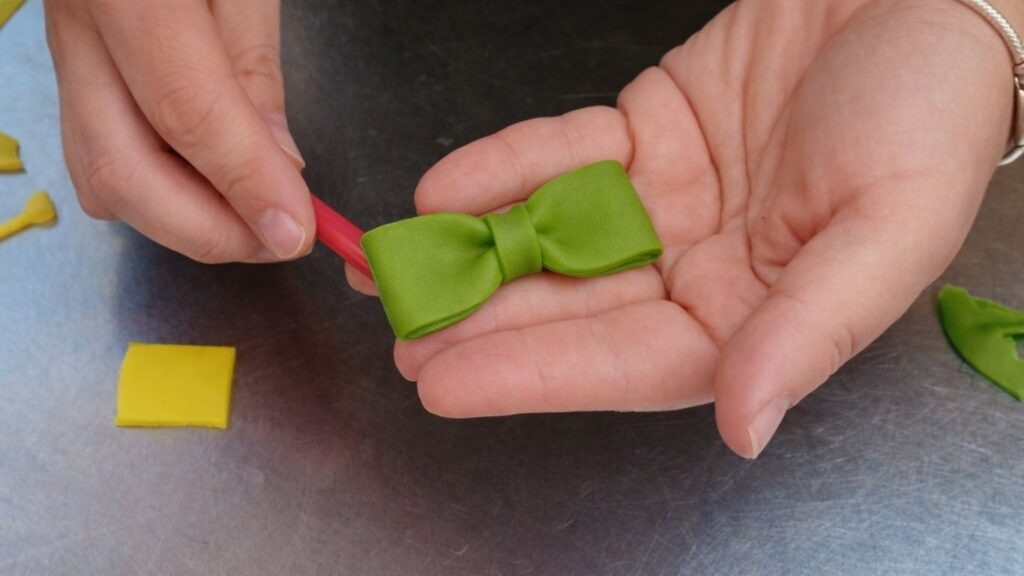 Shaping a fondant bow by folding and pinching strips to decorate the candy cake.