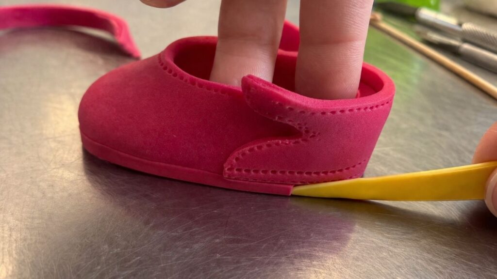 Attaching the back piece to pink fondant baby shoes using water as edible glue