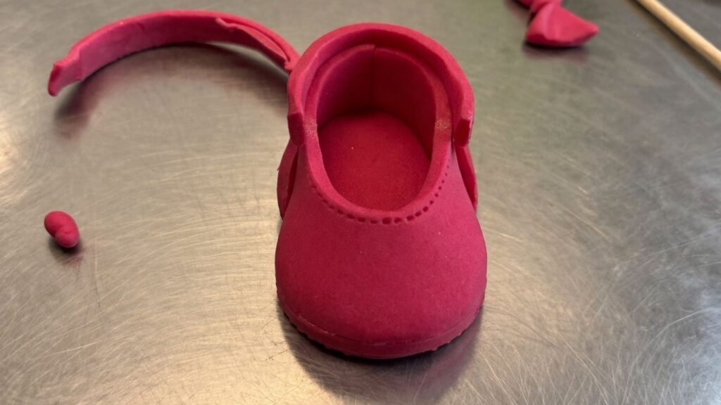 Adding thin fondant strip border around the sole of pink fondant baby shoes for a finished look