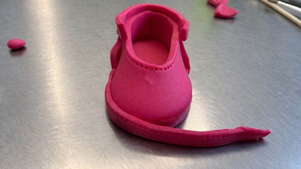 Adding thin fondant strip border around the sole of pink fondant baby shoes for a finished look