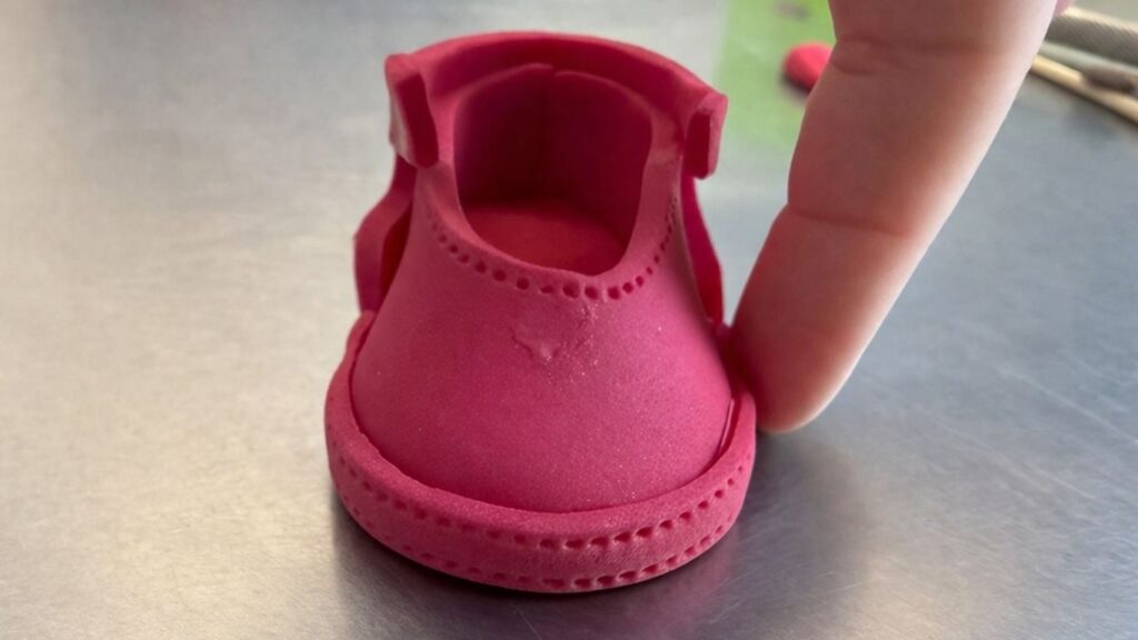Adding thin fondant strip border around the sole of pink fondant baby shoes for a finished look