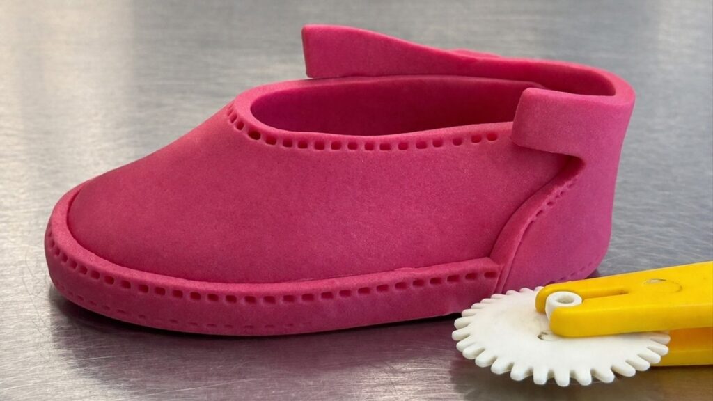 Using stitch tool to add realistic stitch marks along the border of pink fondant baby shoes
