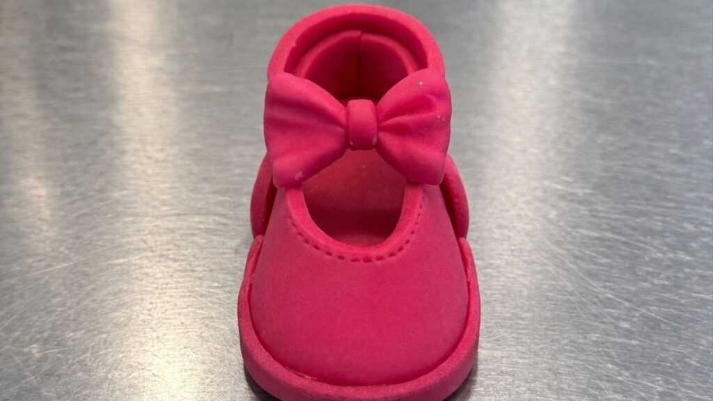 Attaching pink fondant bow on top of fondant baby shoes using water as edible glue