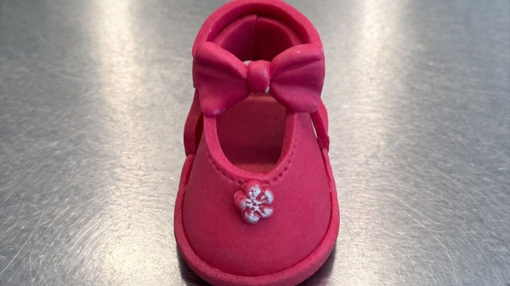 Adding a small fondant flower detail to the front of pink fondant baby shoes for a finishing touch