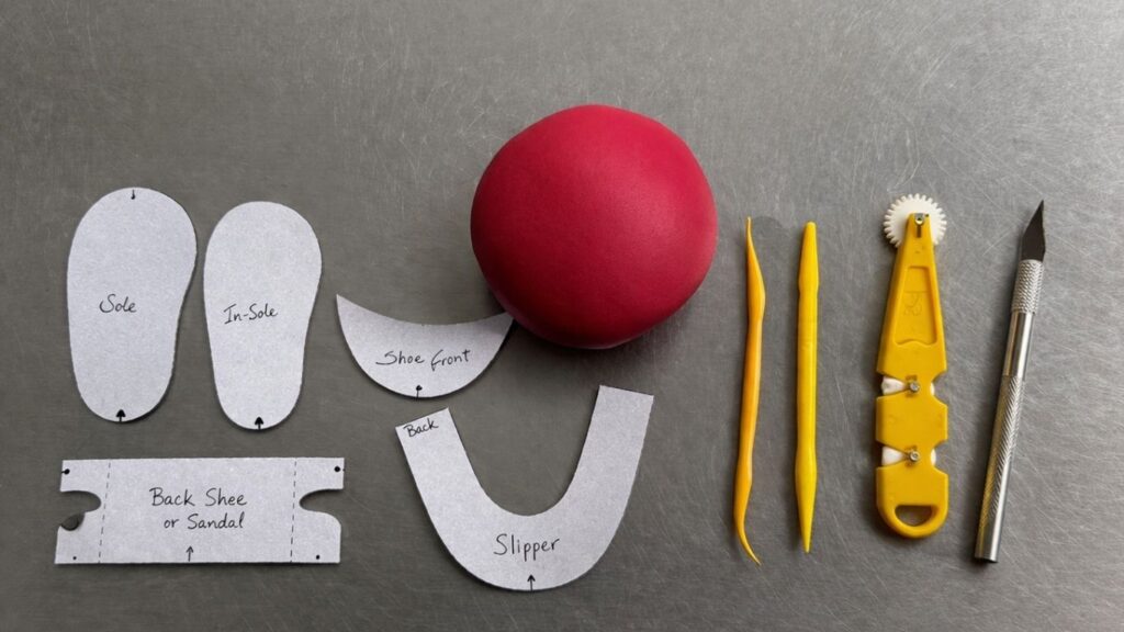 Tools and materials needed to make fondant baby shoes including template, scalpel, modeling tools, stitch tool and pink fondant